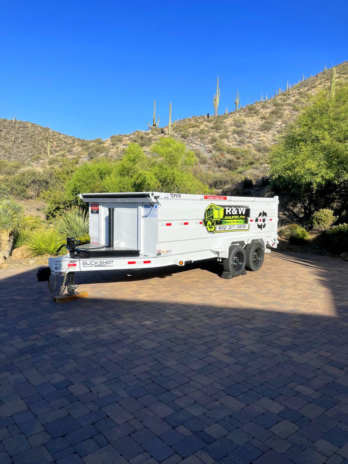 White enclosed R&Y Rentals equipment trailer parked on a brick patio with desert hills and saguaro cacti in the background